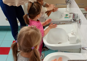 Nauczycielka pomaga chłopcu prawidłowo umyć dłonie.