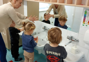Nauczycielka prezentuje dzieciom jak dokładnie umyć przestrzenie międzypalcowe.