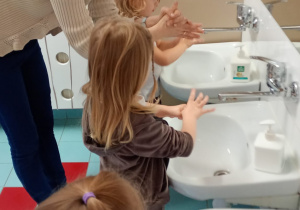 Nauczycielka prezentuje dzieciom jak dokładnie umyć część dłoni w pobliżu kciuka.