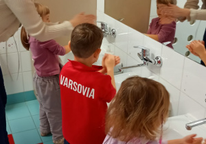 Nauczycielka prezentuje dzieciom jak dokładnie umyć grzbiet dłoni.