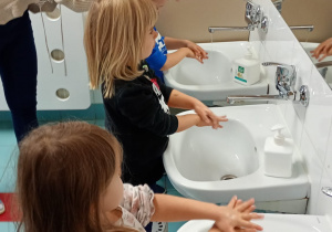 Nauczycielka prezentuje dzieciom jak dokładnie umyć przestrzenie międzypalcowe.