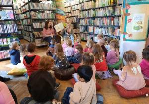 Dzieci uważnie słuchają czytanej przez bibliotekarkę książki.