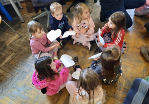 Chłopczyk i sześć dziewczynek siedzi w małym kółeczku, każde z dzieci trzyma w ręku serduszko.