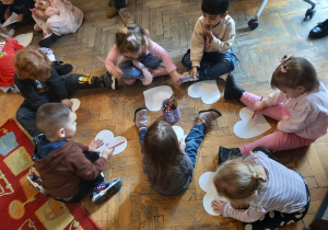 Grupa trzech chłopców i czterech dziewczynek ozdabia kredkami swoje serduszka.