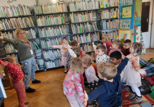 Dzieci wraz z Panią bibliotekarką stoją z szeroko rozłożonymi rękoma na znak ogromnej miłości do swoich rodziców.