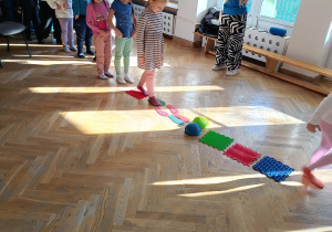 Dzieci stoją ustawione w pociągu i po kolei przechodzą po specjalnej sensorycznej macie.