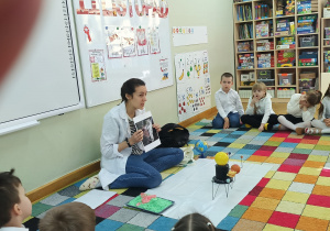 Dzieci siedzą na dywanie, a prowadząca warsztaty prezentuje im zdjęcie kosmonauty.