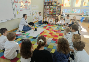 Dzieci siedzą na dywanie, a prowadząca prezentuje im model Układu Słonecznego.