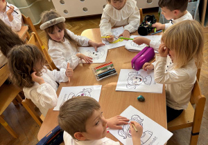 Trzy dziewczynki i trzech chłopców siedzi przy stolikach i koloruje kolorowanki przedstawiające różne emocje.