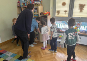 Dzieci wspólnie z prowadzącym zajęcia szukają znaku „CE” na zabawkach w sali.