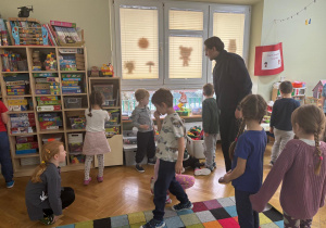 Dzieci wspólnie z prowadzącym zajęcia szukają znaku „CE” na zabawkach w sali.