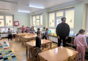 Dzieci wspólnie z prowadzącym zajęcia szukają znaku „CE” na zabawkach w sali.