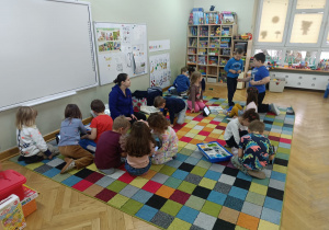 Dzieci podzielone na mniejsze grupki siedzą na dywanie i budują budowle z klocków Lego podczas zajęć z robotyki.