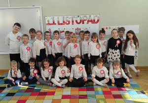 Starsza grupa pozuje do grupowego zdjęcia w galowych strojach na tle dekoracji z okazji 11 listopada.