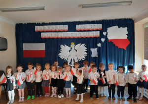 Młodsza grupa pozuje do grupowego zdjęcia w galowych strojach na tle dekoracji z okazji 11 listopada.