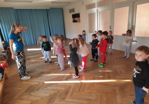 Dzieci stoją w rozsypce na sali gimnastycznej, robią z jednej ręki okulary i przesuwają ją przed oczami.