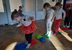 Trzy dziewczynki po kolei przechodzą po sensorycznym torze przeszkód.