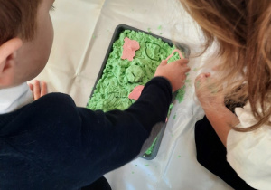 Chłopiec odbija wzór muszelki w zielonym piasku kinetycznym.