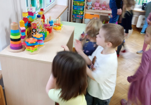 Chłopczyk i trzy dziewczynki szukają serduszek na półce z drewnianymi zabawkami.