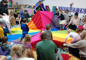 Nauczycielka odsłania wraz z dziećmi pierwszą zabawę, która znajduje się pod chustą.