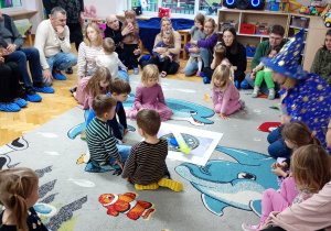 Chłopiec wraz z gromadką dzieci z grupy siedzą wokół planszy i czekają, aż Koło Fortuny się zatrzyma.