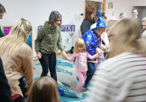 Rodzice, dzieci oraz nauczycielka tańczą w kole wiązanym zbliżając się do jego środka.