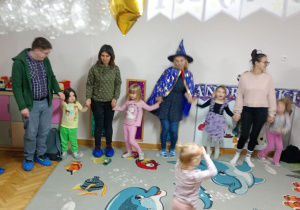 Nauczycielka, rodzice oraz dzieci tańczą trzymając się za ręce.