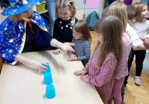 Nauczycielka przeprowadza wróżbę z kubeczkami.