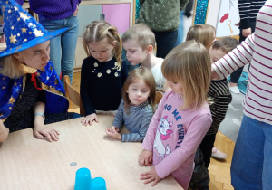 Nauczycielka odsłania wybrany przez dziewczynkę kubeczek, pod którym znajduje się moneta.