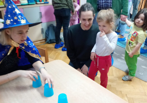 Dziewczynka przygląda się jak nauczycielka przestawia kubeczki.