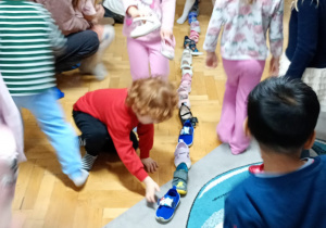 Przedszkolaki ustawiają po jednym buciku w długim rzędzie.