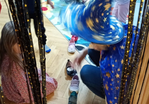 Nauczycielka przekłada bucik przez próg drzwi.