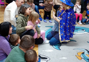 Nauczycielka pokazuje wylosowany przez dziewczynkę kartonik pozostałym dzieciom.