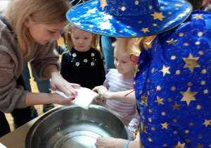 Nauczycielka wyjmuje z wody wlany przez dziurkę wosk i podaje go mamie dziewczynki.