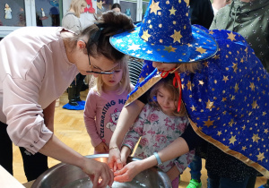 Dziewczynka z pomocą nauczycielki trzyma klucz nad miską z wodą, a jej mama wlewa przez dziurkę wosk.