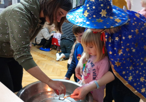 Dziewczynka z pomocą nauczycielki trzyma klucz nad miską z wodą, a jej mama wlewa przez dziurkę wosk.