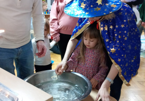 Dziewczynka z pomocą nauczycielki trzyma klucz nad miską z wodą, a jej tata wlewa przez dziurkę wosk.