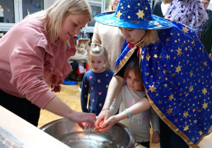 Dziewczynka z pomocą nauczycielki trzyma klucz nad miską z wodą, a jej mama wlewa przez dziurkę wosk.