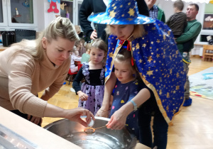 Dziewczynka z pomocą nauczycielki trzyma klucz nad miską z wodą, a jej mama wlewa przez dziurkę wosk.