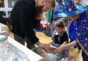 Dziewczynka z pomocą nauczycielki trzyma klucz nad miską z wodą, a jej tata wlewa przez dziurkę wosk.