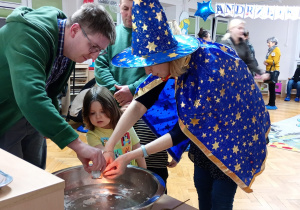 Dziewczynka z pomocą nauczycielki trzyma klucz nad miską z wodą, a jej tata wlewa przez dziurkę wosk.