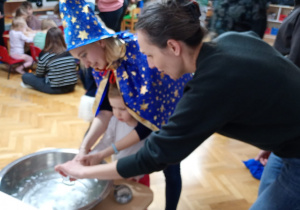 Dziewczynka z pomocą nauczycielki trzyma klucz nad miską z wodą, a jej mama wlewa przez dziurkę wosk.