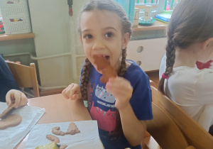 Dziewczynka siedzi przy stoliku i je wykonane samodzielnie pierniczki z gruszką na podwieczorek.