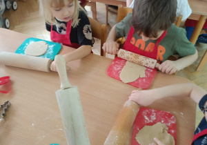 Chłopcy siedzą przy stoliku, rozwałkowują ciasto na pierniczki i wyciskają wybrane przez siebie wzory przy użyciu foremek.