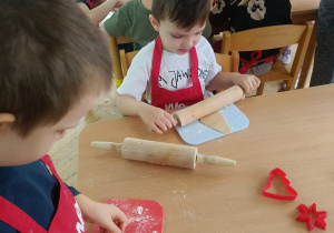 Chłopcy siedzą przy stoliku, rozwałkowują ciasto na pierniczki i wyciskają wybrane przez siebie wzory przy użyciu foremek.