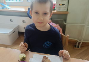 Chłopiec siedzi przy stoliku i je pierniczki wykonane przez siebie i kolegów i koleżanki z grupy na podwieczorek razem z gruszką.