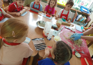 Dzieci siedzą przy stolikach i przygotowują się do robienia pierniczków na zajęciach kulinarnych.