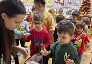 Dzieci stoją ustawione w pociąg i po kolei podchodzą do mamy koleżanki i wybierają zawieszki do swoich ozdób choinkowych.