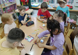 Dzieci siedzą przy stolikach i markerami dekorują drewniane i styropianowe dekoracje świąteczne wg. własnego pomysłu.