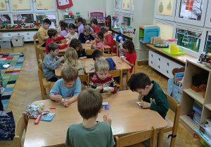 Dzieci siedzą przy stolikach i markerami dekorują drewniane i styropianowe dekoracje świąteczne wg. własnego pomysłu.